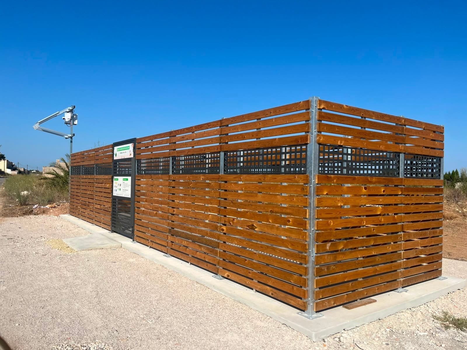 Recinte d’una àrea d’aportació, tancat amb llistons de fusta i amb càmera de videovigilància
